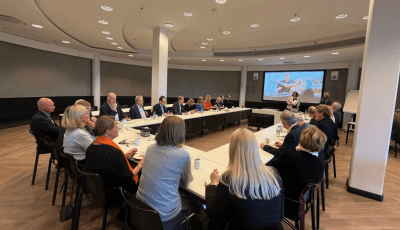 Boardmanin vieraily Yleisradioon. Yleisöä pöydän ääressä ja puhuja heidän edessään.